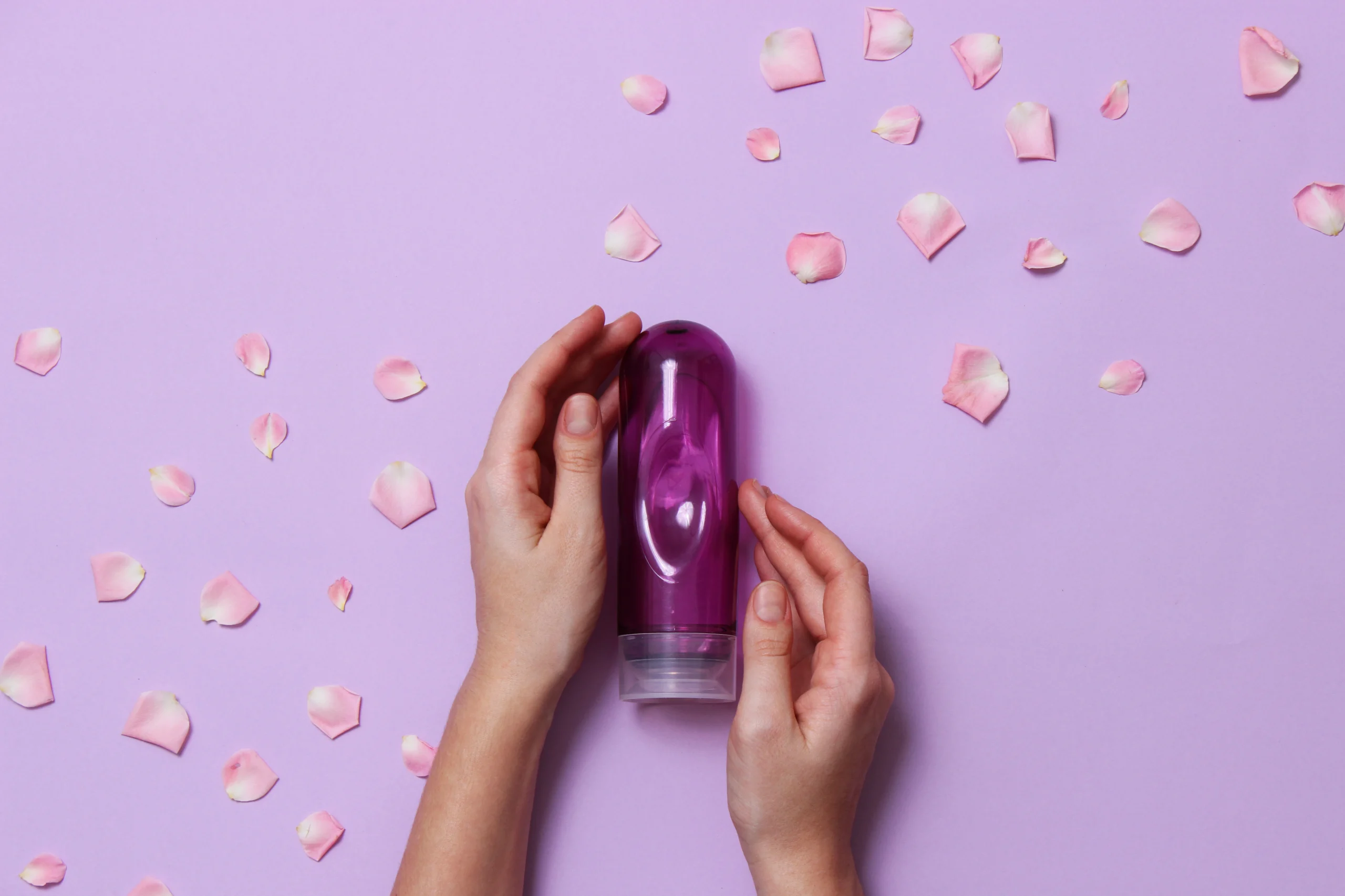 Lubricant surrounded by rose petals on a pink background; for artlcle "What is Cannabis Lube?"